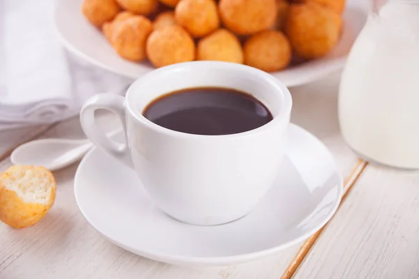 Cup of coffee with small balls of freshly baked homemade cottage cheese doughnuts in a plate on a background. — Stock Photo, Image