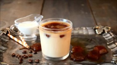 Buz küpleri ve kahve çekirdekleri ile buzlu soğuk latte kahve. Kadının eli metal tepsiye buzlu kahve ile cam koyar.