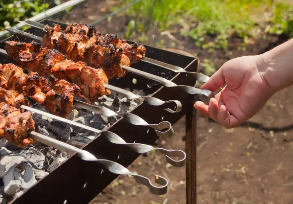 On the barbecue, a lot of meat is roasted on skewers, the chef turns over his shish kebabs. A man\'s hand turns, fries tasty meat of pork on skewers.