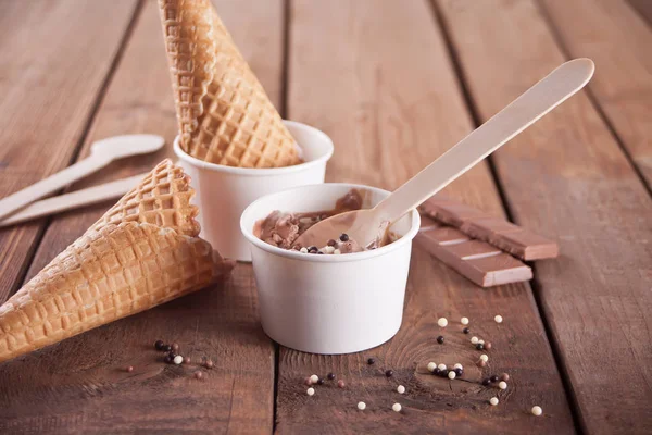 Ciotole di carta di gelato al cioccolato con coni di cialde e cucchiai di legno sullo sfondo di legno — Foto Stock