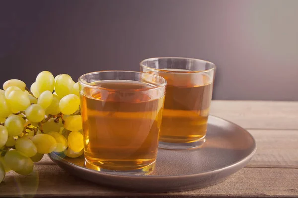 Glass of green grape juice or white wine with bunch of grape on the wooden background.