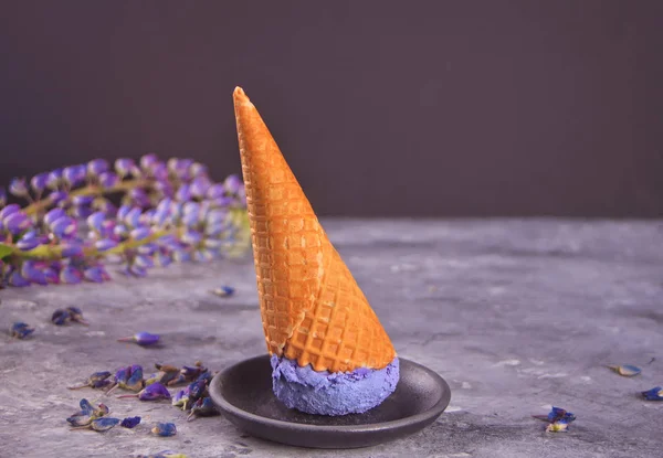 Cono de gofre con helado lila púrpura sobre el fondo gris oscuro adornando altramuces — Foto de Stock