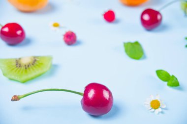 Mavi arka planda dağınık kiraz meyveleri, kivi, çilek ve nane yaprakları.