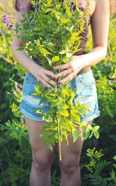 Mujer joven vestida de blanco en un prado. Ella está de pie con ramo de flores silvestres en sus manos . —  Fotos de Stock