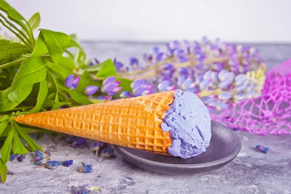 ルピインを飾るダークグレーの背景に紫色のライラックアイスクリームとワッフルコーン — ストック写真