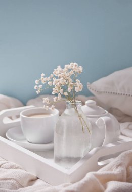Beyaz tepside çay, süt, çaydanlık ve beyaz çiçek buketi fincan yakın.