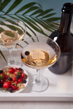 Beyaz ahşap tepsi üzerinde çilek ile bir gözlük, şişe ve plaka beyaz şarap. İki kişi için akşam yemeği.