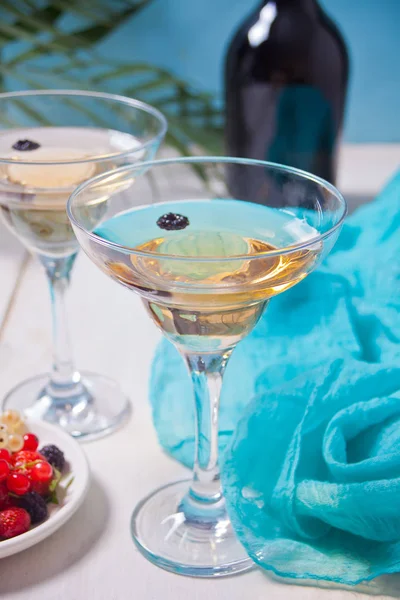 Witte wijn in een glazen, fles en bord met bessen op de witte houten tafel. Diner voor twee. — Stockfoto