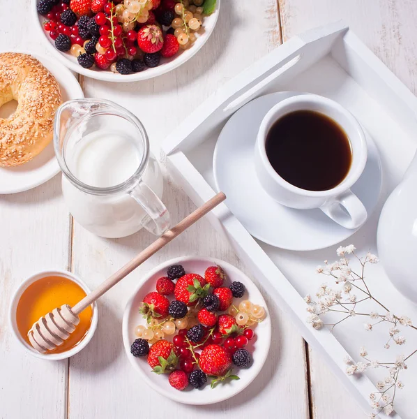 Fresh sweet berries on the white plate, bagel, cup of coffee and honey for breakfast. — Stock Photo, Image