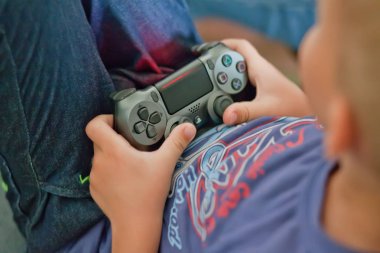 Siyah konsol ped kumandası joystick tutan ve oyun oynayan bir erkek çocuk eller. Havai görünüm.