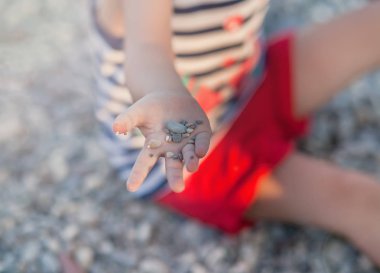 Sahilde elinde küçük taşlar tutan küçük kız.