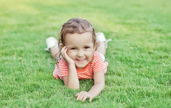 Portret uśmiechniętej dziewczynki leżącej na zielonej trawie. — Zdjęcie stockowe