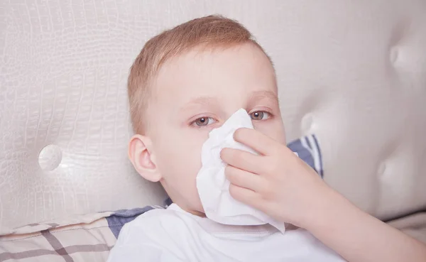 Anak sakit berbaring di tempat tidur dan meniup hidungnya — Stok Foto
