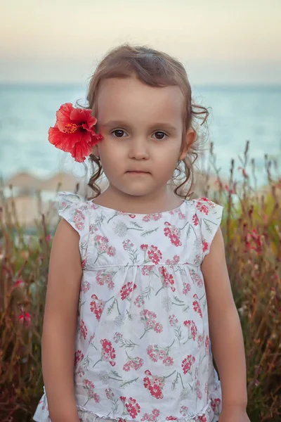 Маленька дівчинка з червоною квіткою за її вухом — стокове фото