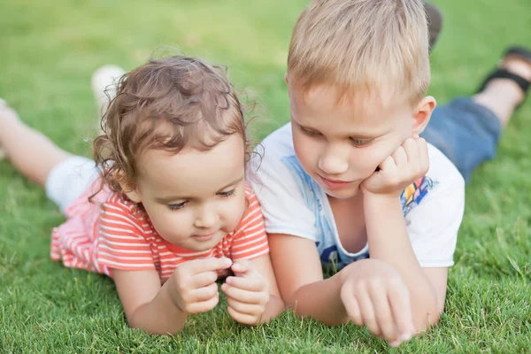 緑の草の上に横たわっている笑顔の小さな女の子と少年の肖像画. — ストック写真