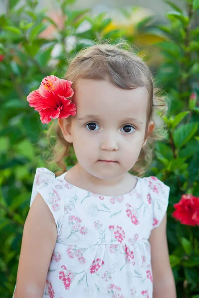 Menina criança com flor vermelha atrás de sua orelha — Fotografia de Stock