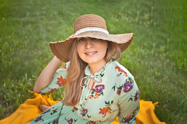 黄色い毛布の上に座ってピクニックの女性は、彼女の帽子を保持し、楽しんで — ストック写真