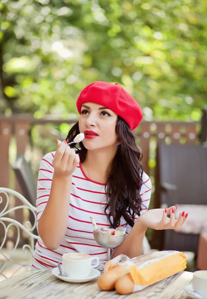 Mulher com uma camisa listrada e boné vermelho comendo sorvete em um café . — Fotografia de Stock