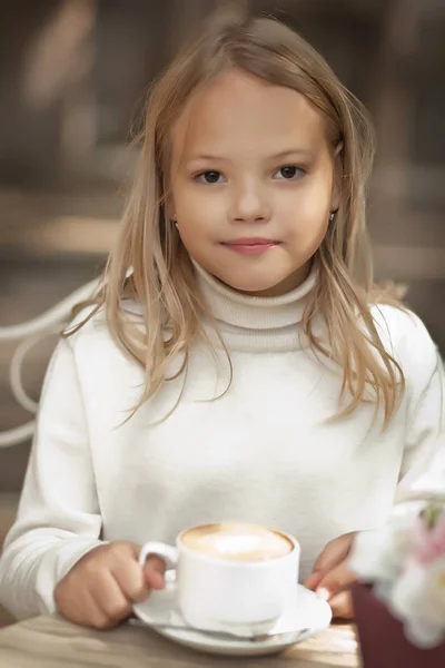 Linda niña sonriendo y bebiendo capuchino en la cafetería al aire libre —  Fotos de Stock