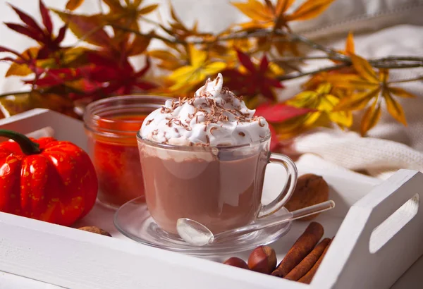 Чашка горячего сливочного какао с пеной на белом подносе с осенними листьями и тыквами на заднем плане — стоковое фото