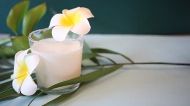 Kadın eli çiçek plumeria ve palmiye yaprağı ile masaya hindistan cevizi sütü cam koymak.