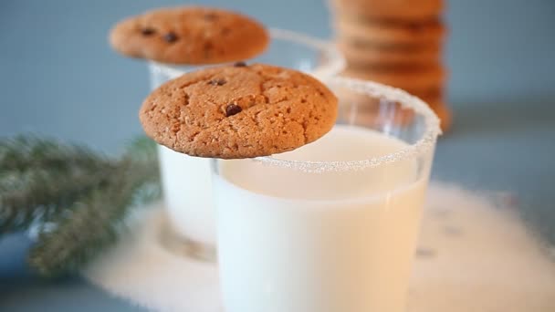女性の手はミルクのグラスからクリスマスクッキーを取ります 背景にクリスマスツリーブランチ — ストック動画