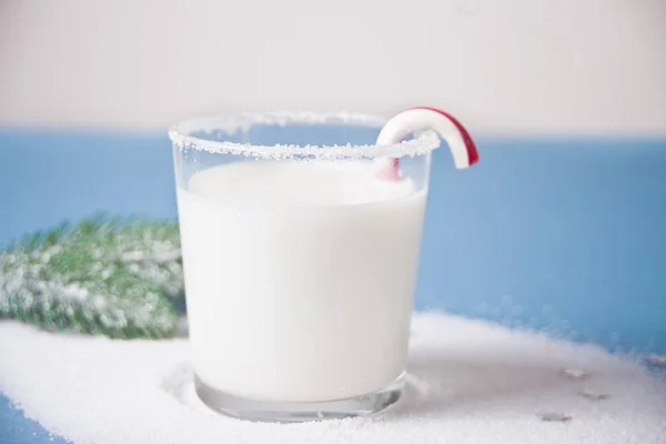 Glass of milk, candy cane, christmas tree branch on the blue background