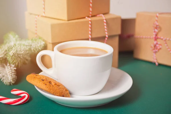 Чашка чаю, домашнє печиво, різдвяні подарункові коробки та різдвяний декор на зеленому фоні . — стокове фото