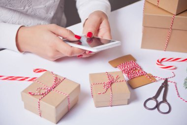 Noel hediyesi süslemesi. El yapımı dekor konsepti. Kadın hediye paketi. Telefona bakan kadın.