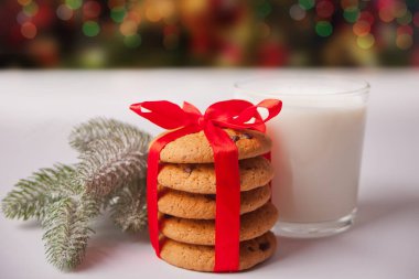 Beyaz masada bir bardak süt, kurabiye ve çam dalı.