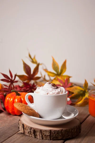 Чашка горячего сливочного какао с пеной с осенними листьями и тыквами на заднем плане — стоковое фото