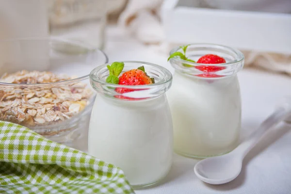 Duas porções de iogurte caseiro natural em um frasco de vidro com morango fresco e muesli nas proximidades — Fotografia de Stock
