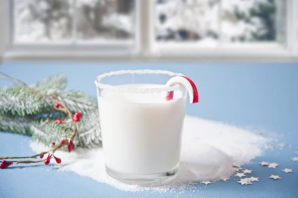 一杯牛奶、甘蔗、圣诞树枝条在蓝色背景的寒冷冬日的窗上 — 图库照片