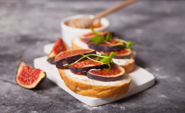 Krem peynirli sandviç, incir ve bal küçük beyaz bir kesme tahtasında servis ediliyor. Sağlıklı gıda konsepti