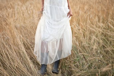Buğday tarlalarında beyaz elbiseli ve siyah çizmeli genç bir kadın. Kaba bir düğün olacak..