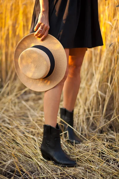 若いです黒のドレスで立っているフィールドに小麦と彼女の手に帽子を保持 — ストック写真