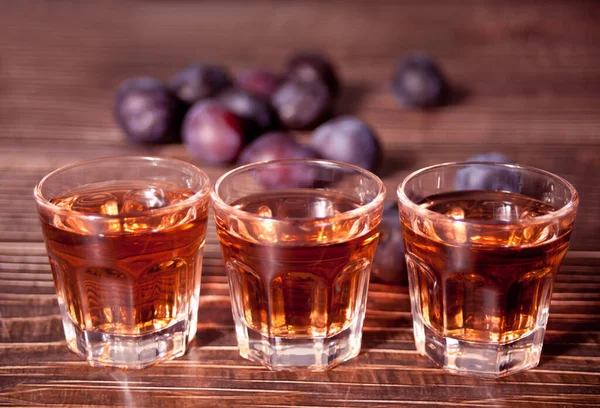Wódka lub brandy ze świeżymi śliwkami na drewnianym stole. — Zdjęcie stockowe