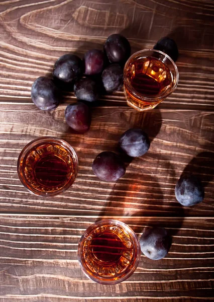 Plum vodka or brandy with fresh plums on the wooden table. Top view.