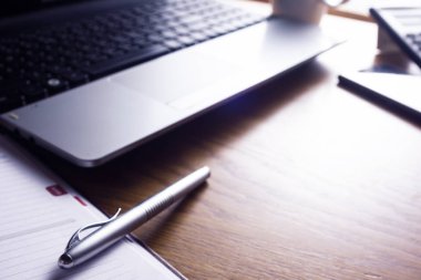Dizüstü bilgisayar, ajanda, kalem, telefon ile bir resepsiyon çalışma alanı gösterilen yüksek çözünürlüklü görüntü.