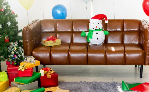 Snowman on the sofa with a gift box and Christmas tree