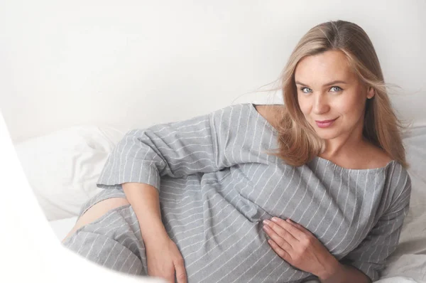 Mujer embarazada feliz tumbada en una cama en casa —  Fotos de Stock
