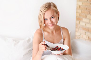 Güzel genç sarışın kadın uyanma ve sabah çilek ile yulaf ezmesi yeme.