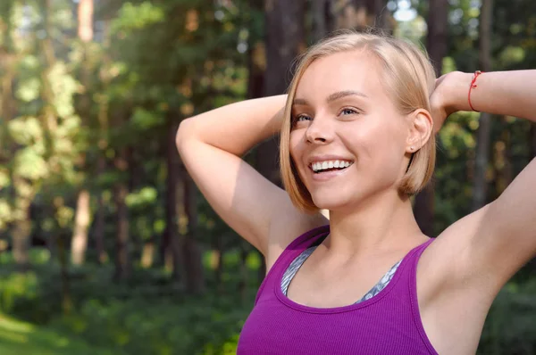 Portrait of young smilling sporty woman stretching in the fores outdoor early in the morning — Stock Photo, Image