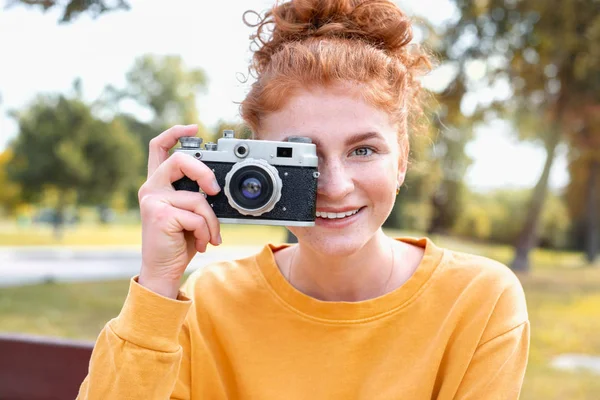 Smiling happy red hair student girl taking picture with old vintage camera outside in autumn park — Stock Photo, Image