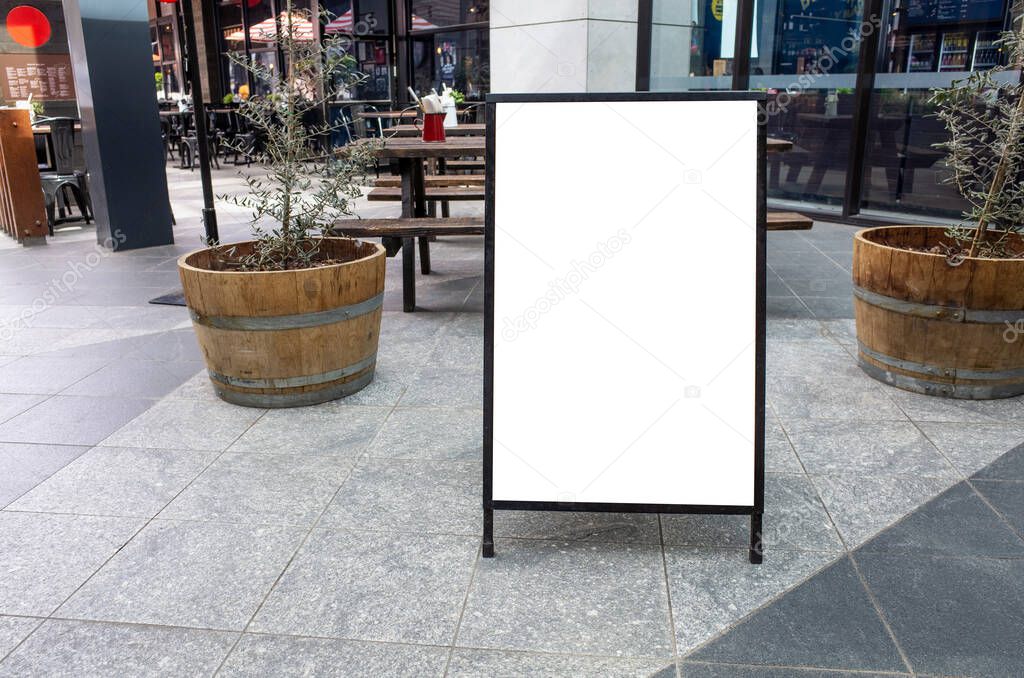 Blank white outdoor advertising stand/sandwich board mockup template. Clear street signage board placed by an outdoor dining area of a restaurant. Background texture of standee on the street.