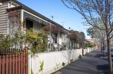  A row of weatherboard houses with Victorian-era wrought iron lacework and wooden fence in an Australian suburb. clipart