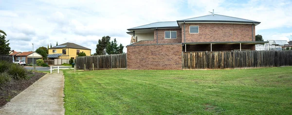 Panoramic view of a vacant land next to a two-story residential house. Wide angle suburban view in an Australian residential neighbourhood. Mown lawn grass in a public nature reserve in a suburb.