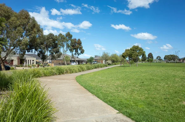 遠くにいくつかの近代的なオーストラリアの家 家と郊外の公園で湾曲した歩行者用歩道 大きな芝生とオープンスペースで地元の公園の背景テクスチャ テキストのコピースペース — ストック写真