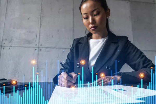 A woman signs contract and financial chart hologram. Concept of stock market analysis. Multiexposure. International business.