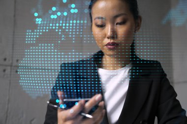 İş kadını telefonu kullanıyor, modern ofiste yeni bir proje üzerinde çalışıyor. Çifte maruziyet. Başarı kavramı. Dünya haritası Dünya hologramı.